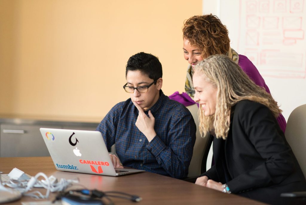 trois femmes à côté d'une table regardant un MacBook.